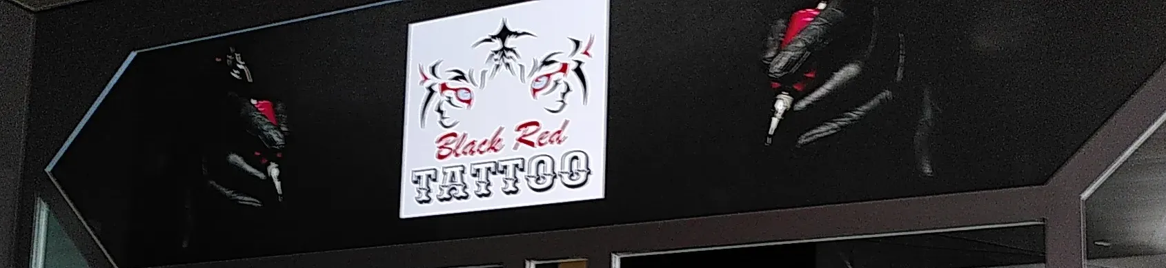 Schild von Black Red Tattoo mit dem Logo aus zwei Gesichtern und roten Augen, daneben Tattoomaschinen auf schwarzem Glas